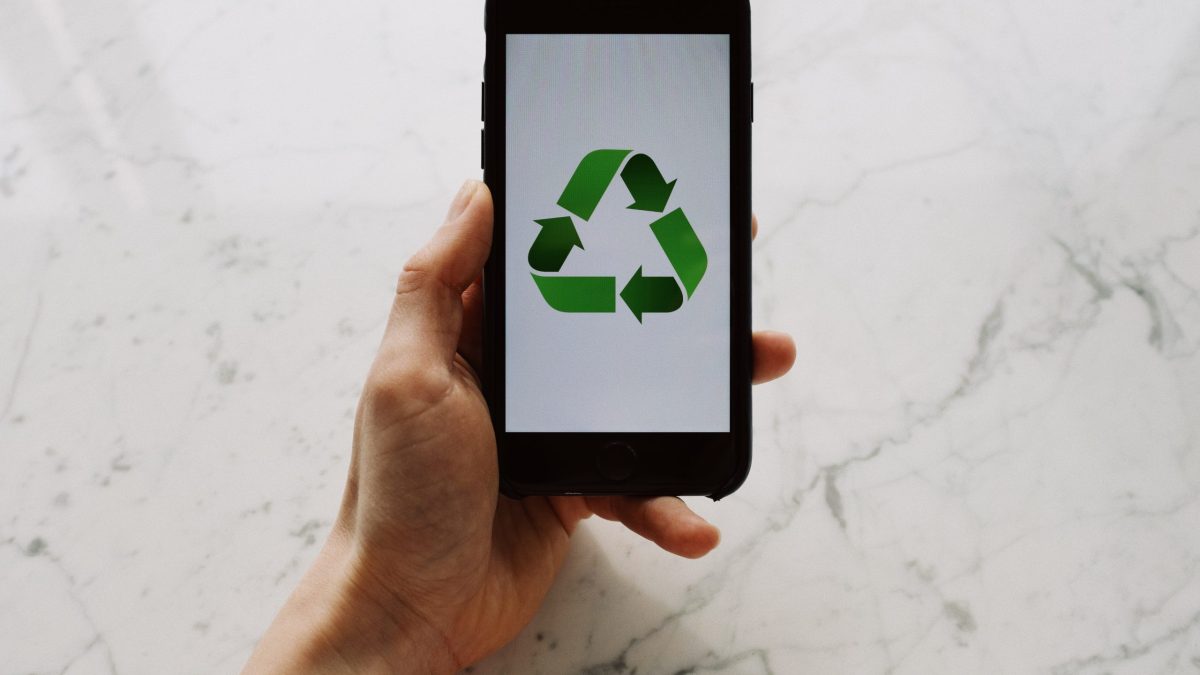 From above view of faceless person holding mobile phone with white screen and green recycle logo above marble surface