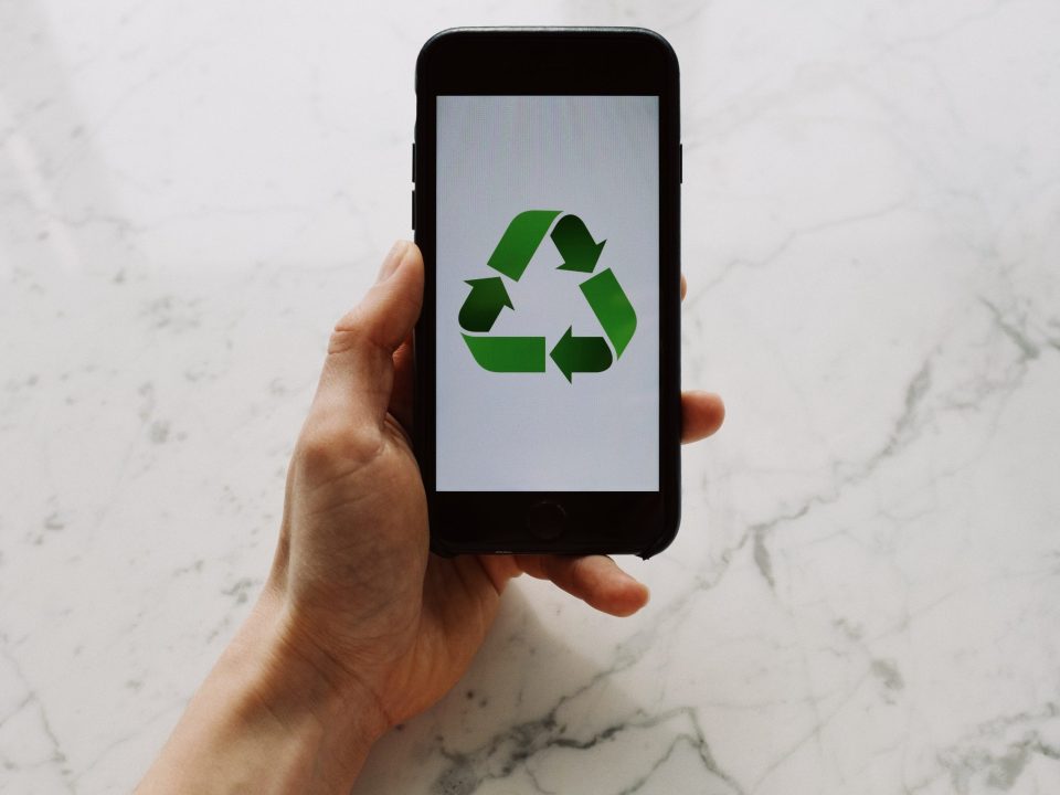 From above view of faceless person holding mobile phone with white screen and green recycle logo above marble surface