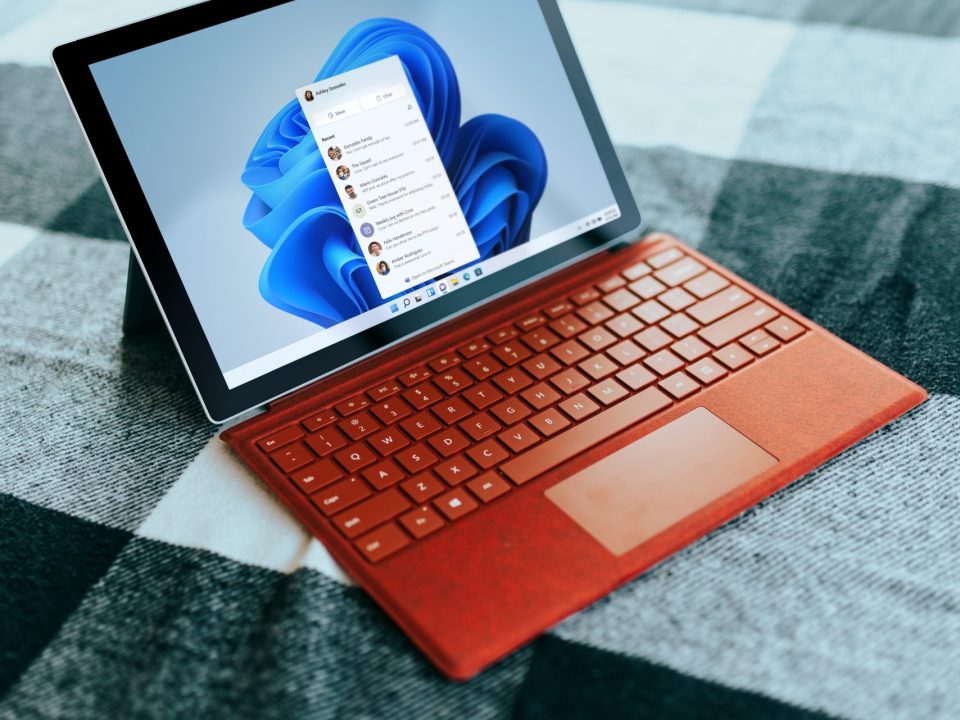 Red Surface laptop on a checkered bed by a window